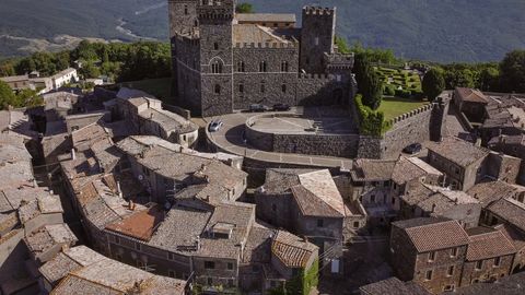 Luftaufnahme des Schlosses vom Dorf aus, mit historischen Steinhäusern vor der Wehrmauer. im-58791670.jpeg