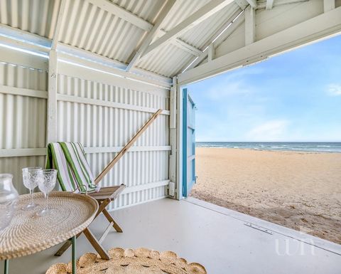 Eingerichtete Sitzecke mit Rattanstuhl, Teppich und kleinem runden Esstisch, mit weit geöffneten Türen direkt zum Strand. 2020482416_2_1_251211_023309-w1123-h900.jpeg