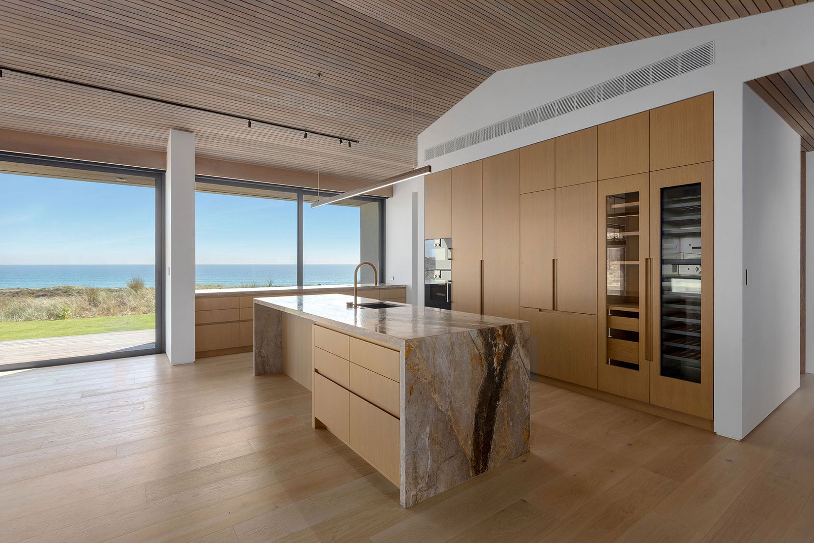 Helle Holzküche mit großzügiger Marmorkücheninsel und raumhohem Panoramafenster mit direktem Zugang zum Strand und Blick aufs Meer. Te-Arai-Homesite-3.jpg