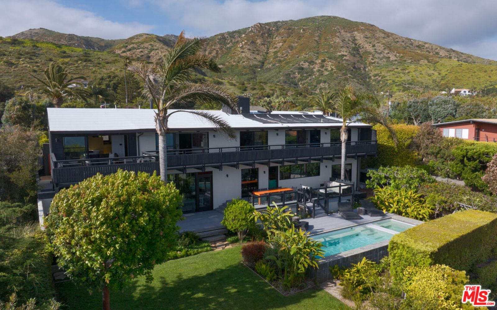 Luftaufnahme einer zweistöckigen Villa über dem Garten, umgeben von Palmen und mit sanften Hügeln im Hintergrund im Tageslicht origin3.jpeg