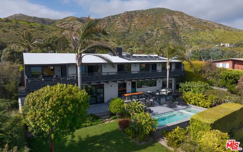 Luftaufnahme einer zweistöckigen Villa über dem Garten, umgeben von Palmen und mit sanften Hügeln im Hintergrund im Tageslicht origin3.jpeg