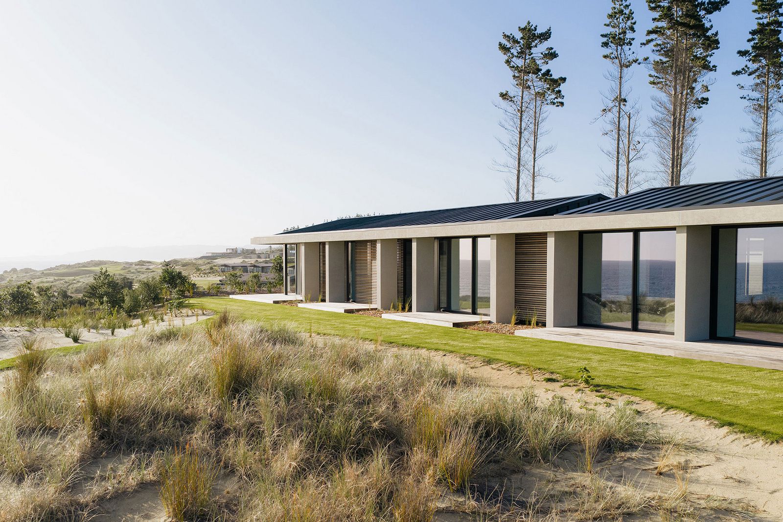 Vom Strand aus sichtbares Haus mit großflächigen Fenstertüren, die das Meer spiegeln. Te-Arai-Homesite-6.jpg