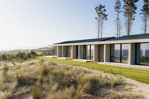 Vom Strand aus sichtbares Haus mit großflächigen Fenstertüren, die das Meer spiegeln. Te-Arai-Homesite-6.jpg