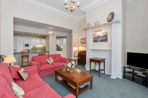 Wohnzimmer mit zwei rosafarbenen Sofas, Holztisch und offenem Übergang zur weißen Küche mit Frühstückstheke. Hohe Decken und klassische Details prägen den Raum. 53152206.jpg