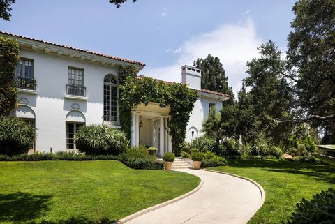 Weiße Villa im mediterranen Stil mit Säulenportal, begrüntem Eingangsbereich und geschwungener Zufahrt durch einen gepflegten Garten. 1900xxsxm.jpg