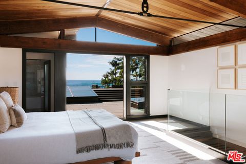 Schlafzimmer mit Bett vor einer Treppe ins Untergeschoss und weit geöffneter Fenstertür zur Holzterrasse mit Meerblick. origin7.jpg