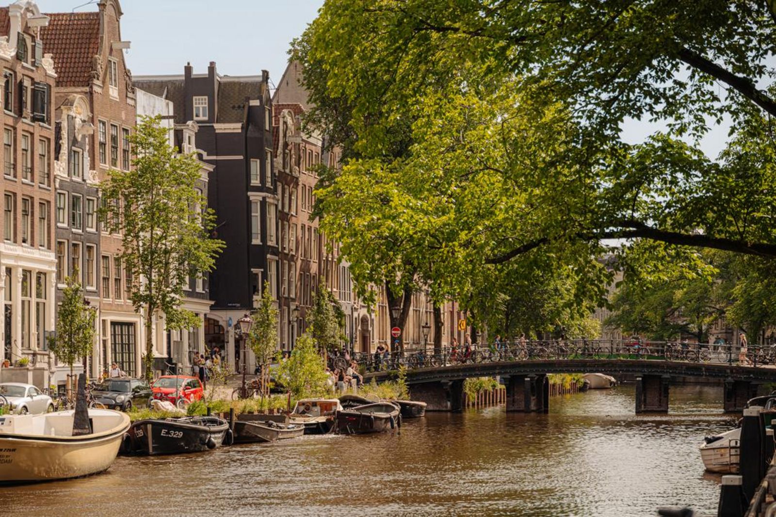Amsterdamer Kanal bei Tageslicht mit Holzkajaks und einer Brücke voller Fahrräder. 245161446.jpg