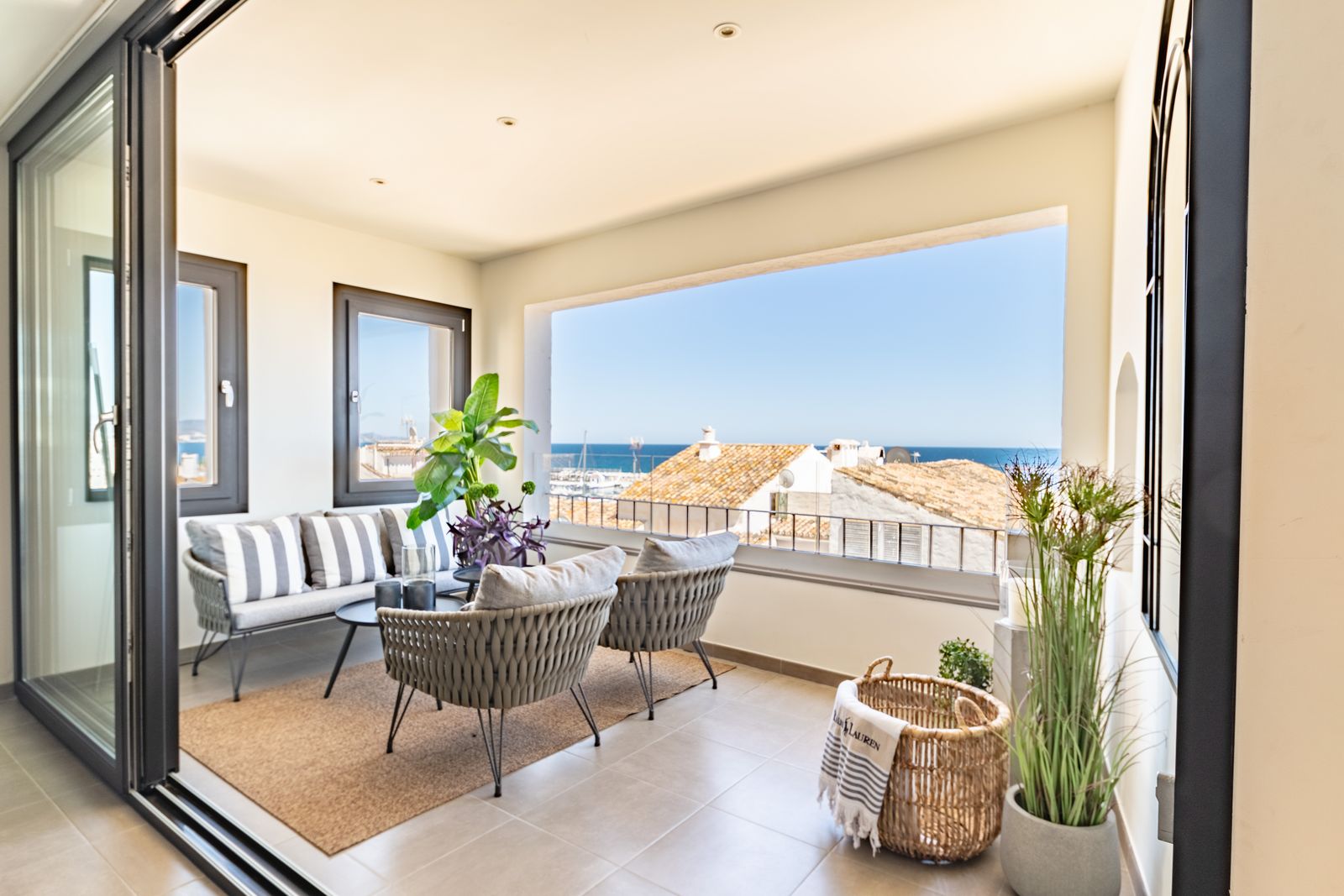 Veranda mit gemütlicher Sitzecke und Blick durch die Fenster auf gegenüberliegende Häuser und das Meer. AdobeStock_1241589666__josehidalgo87.jpeg