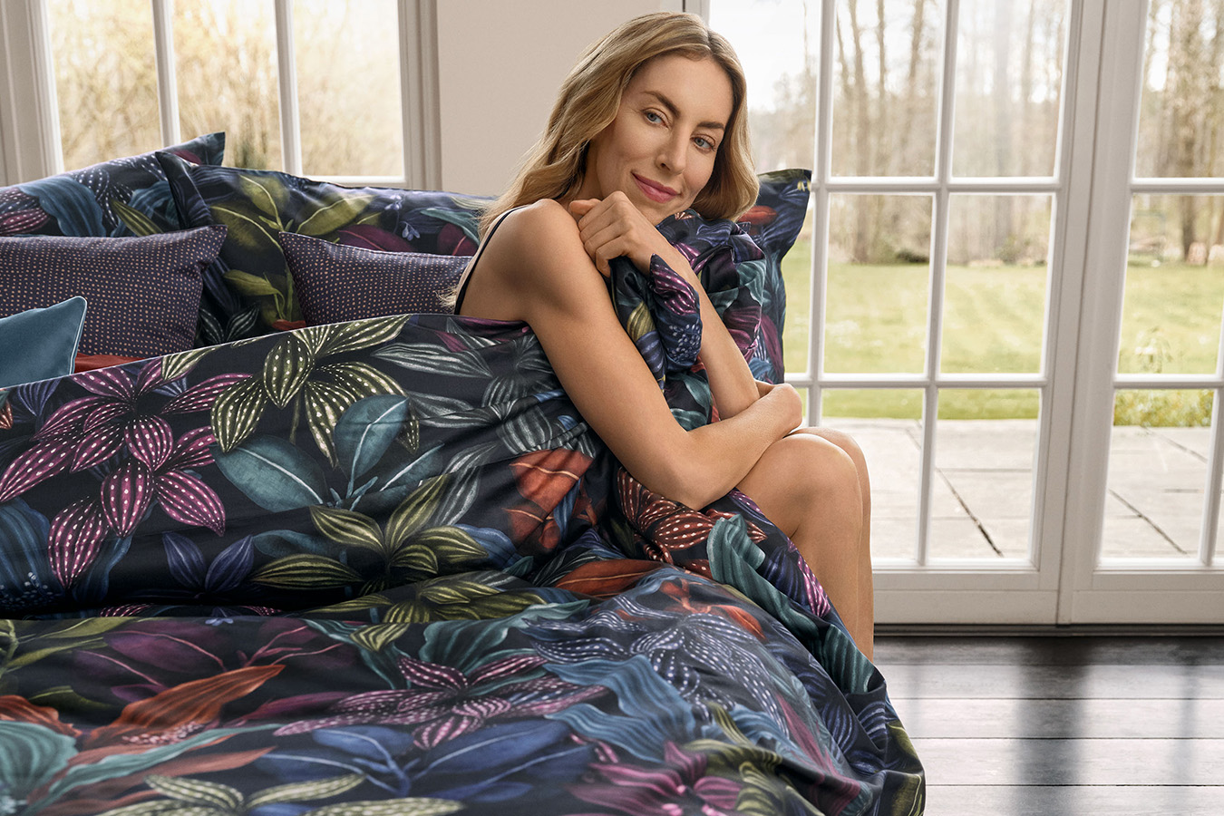 Frau in dunklblaue Bettwäsche mit Mustern gehüllt, sitzt auf Bettkante 1350x900_Website_StilDesign_Bettwa__sche__c_Schlossberg_2.jpg