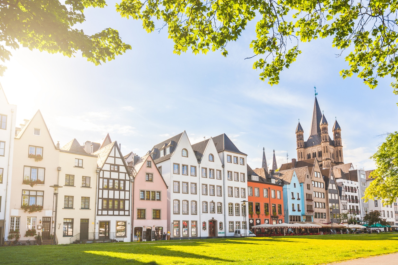 Houses and park in Cologne, Germany. Many of them are colourful, they are facing a public park with green grass and some trees. There is a bell tower on background. Travel and architecture concepts. AdobeStock_101716547_william87.jpeg